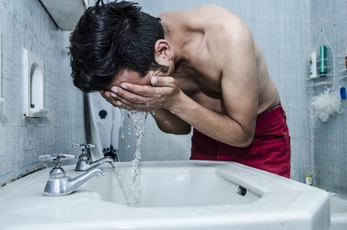 洗面台で顔を洗う男性